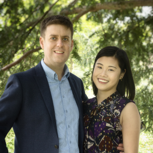 A white man and an asian woman pose and smile for the camera.